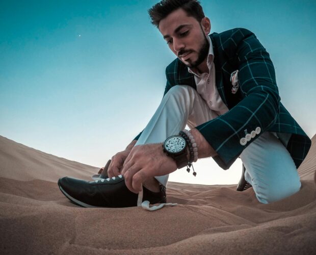 Stylish man tying sneakers in the Dubai desert. Captured at daytime showcasing fashion and lifestyle.
